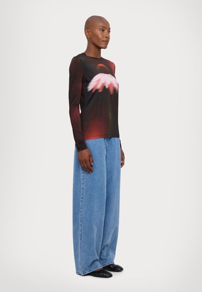 Camicia nera a maniche lunghe con stampa floreale rossa e bianca, abbinata a jeans blu chiaro a gamba larga e scarpe nere. Tessuto morbido e vestibilità comoda.