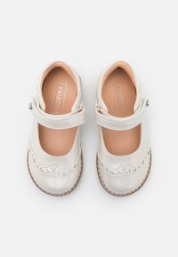 White leather shoes with a rounded toe, scalloped edge, and small heart cutouts. Features a Velcro strap and beige inner lining.