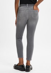 Graue Denim-Slim-Fit-Jeans mit einem mittelhohen Bund, zwei Gesäßtaschen und Seitennähten. Kombiniert mit schwarzen, glänzenden Slippern.