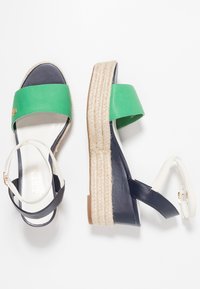 Gröna och marinfärgade lädersandaler med platå och en vävd jutesula. Har ett bredare grönt rem och en smal ankelsnodd i vitt.