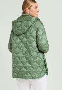 Kurtka puchowa w kolorze zielonym, pikowana, z kapturem, z charakterystycznym wzorem w romby, ściąganym w pasie oraz z zatrzaskiem u dołu. Lekka i wodoodporna.