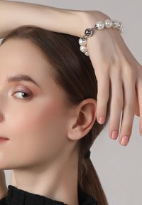 White pearl bracelet with silver accents, featuring a round clasp. Smooth texture, with a classic round shape and glossy finish.