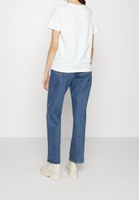 Vit bomullströja, blå denimjeans och beige ankelskots. T-shirten har rund hals, och jeansen har rak passform med lätt blekning.