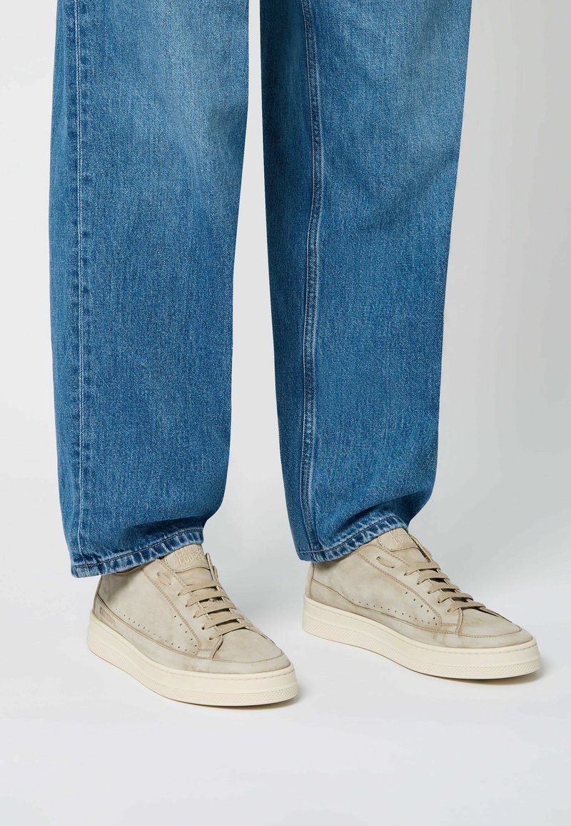 Sneaker in suede beige con suole in gomma chiara, dotate di punta arrotondata, design forato e lacci, abbinate a jeans azzurri.