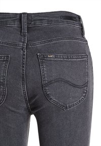 Czarne dżinsy typu denim z lekkim przetarciem, wyposażone w dwie tylne kieszenie, małą metkę z logiem oraz kontrastowe przeszycia wzdłuż szwów.