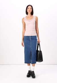 Light pink ribbed tank top with lace trim, paired with a blue denim midi skirt featuring a front slit. Black tote bag and platform shoes.