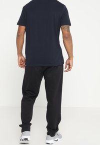 Marinblå t-shirt med kort ärm i kombination med svarta sweatpants. Modellen bär grå fritidsskor och visar upp en avslappnad passform och en avslappnad stil.