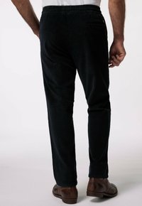 Pantalons en velours côtelé sombre avec une taille élastique, présentant de fines côtes verticales, une poche arrière, et des chaussures en cuir marron.