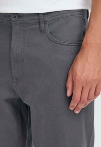 Close-up of a person’s hand resting beside dark gray pants with a button and pocket details visible.