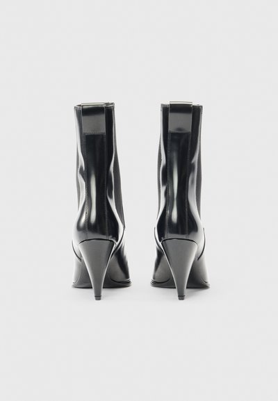 Czarne skórzane botki na obcasie z wysmukłym noskiem, wąskim obcasem i gładkim, błyszczącym wykończeniem. Posiadają wysokie wycięcie na kostkę z delikatnymi detalami stębnowania.