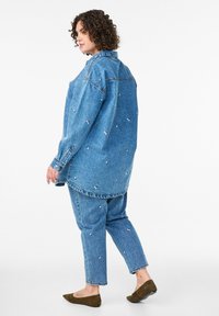 Denimski komplet sestavljen iz ohlapne, svetlo modre srajce in ustreznih kavbojk z majhnimi cvetličnimi vezeninami. Mehka tekstura, sproščen dizajn.