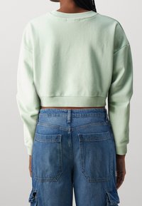 Felpa verde menta cropped con scollatura rotonda e orlo a costine, abbinata a pantaloni cargo in denim blu a vita alta con quattro tasche.