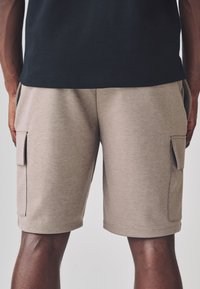 Pantaloncini cargo beige realizzati in tessuto leggero, con tasche laterali, vestibilità comoda e orlo semplice senza motivi visibili.