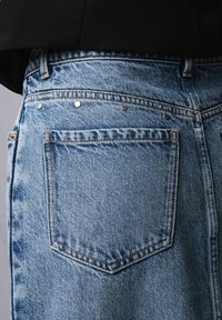 Lys blå denim jeans med en baglomme, med sølvnitter langs skridtet og tekstureret stof. Klassisk fem-lomme design.