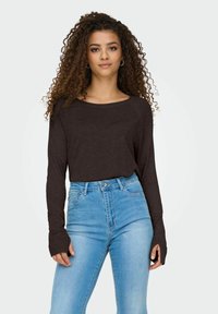 Blusa marrón de manga larga en tejido ligero, con un escote amplio. Combinada con jeans de tiro alto en azul claro, con un diseño clásico de cinco bolsillos.