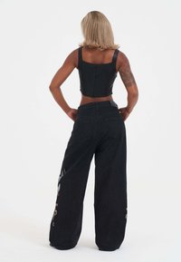 Top corto negro combinado con unos vaqueros de pierna ancha de cintura alta. Los vaqueros presentan acentos bordados en las piernas y un acabado texturizado.