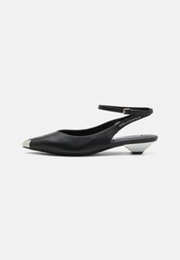 Fekete slingback cipő sima bőrből, hegyes orral és fémes orrheggyel. Alacsony geometrikus sarokkal és bokapánttal rendelkezik.