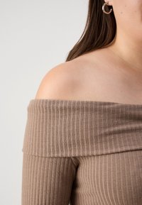 Barna bordázott off-shoulder felső, puha tapintással. Széles dekoltárral és varrás nélküli dizájnnal rendelkezik, amelyet a hozzá illő bordázott anyag egészít ki.