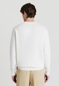 Felpa con texture crema caratterizzata da un collo girocollo a costine, maniche lunghe e un motivo a righe orizzontali sulla parte posteriore. Abbinata a pantaloni beige.