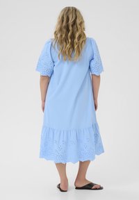 Lichtblauwe jurk tot de knie met oogjesdetails op de korte mouwen en onderzoom, voorzien van een ontspannen pasvorm en een gerimpelde onderrand.
