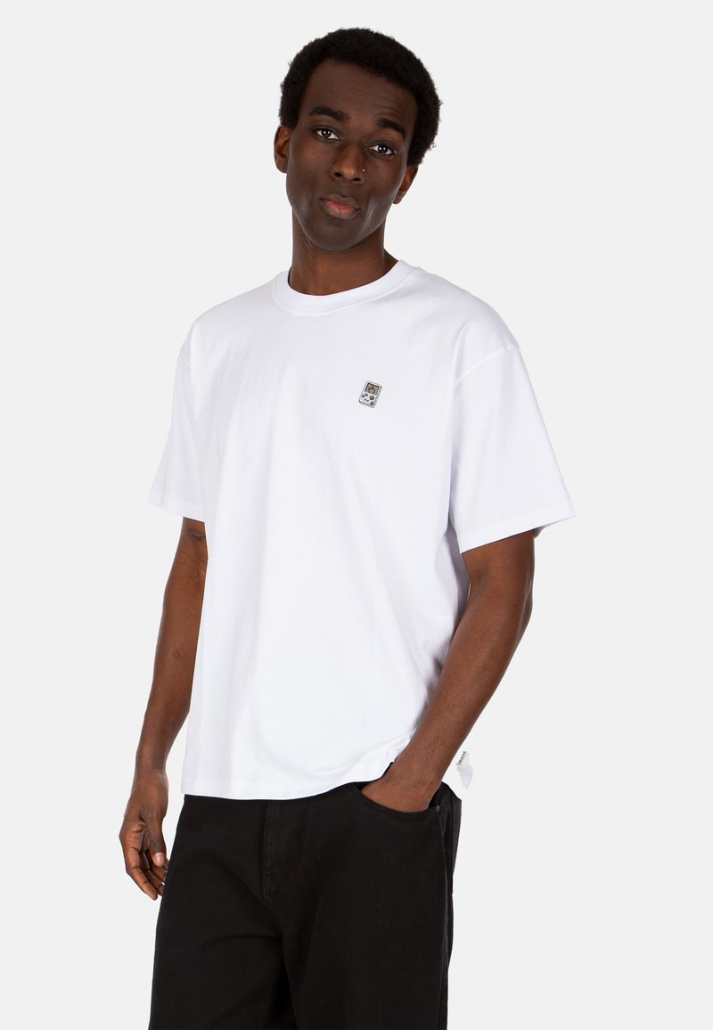 White cotton t-shirt with a round neckline and short sleeves, featuring a small patch logo on the left chest. Black pants with pockets.