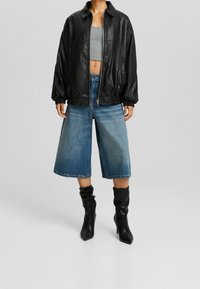 Černá umělá kožená bunda na zip s uvolněným střihem. Šedý krátký top, modré denimové culottes a černé vysoké boty na podpatku. Hladké textury.
