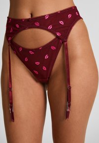 Κόκκινη ζώνη ζαρτιέρας με διάφανο δίχτυ και κεντητό μοτίβο με ροζ χείλη. Διαθέτει ρυθμιζόμενους ιμάντες και διακοσμητική κυματιστή λεπτομέρεια για επιπλέον κομψότητα.