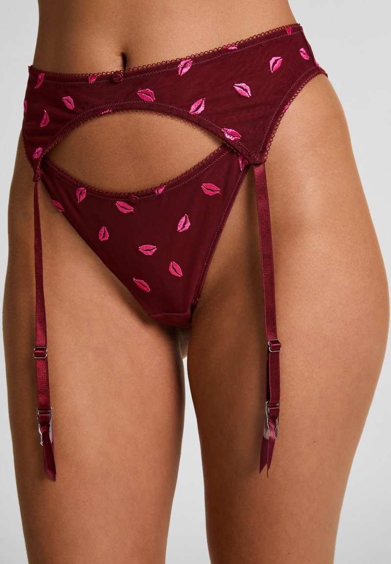 Κόκκινη ζώνη ζαρτιέρας με διάφανο δίχτυ και κεντητό μοτίβο με ροζ χείλη. Διαθέτει ρυθμιζόμενους ιμάντες και διακοσμητική κυματιστή λεπτομέρεια για επιπλέον κομψότητα.