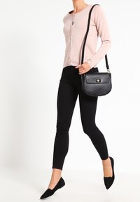 Ljusröd knäppbar kofta, svarta figurnära byxor, svart handväska med spänne och svarta spetsiga ballerina skor. Släta texturer och enkel design.