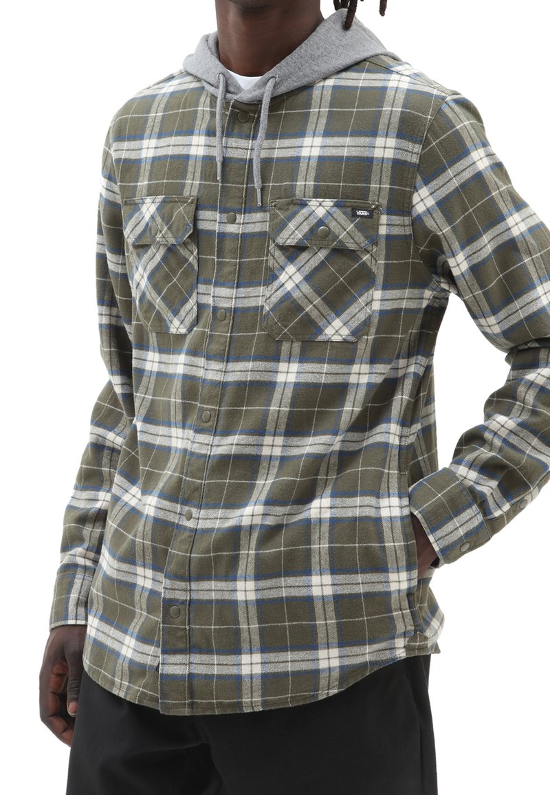 Chemise à manches longues à carreaux dans des tons vert olive, gris et bleu, avec une capuche grise, deux poches poitrine et une fermeture à bouton sur le devant.