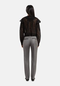 Zwarte kanten top met gerimpelde mouwen, uitsnede op de rug, gedragen over grijze op maat gemaakte broek met achterzakken en geplooide details.