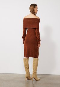 Rostfärgad, off-the-shoulder stickad klänning med långa ärmar och figurnära silhuett. Matchad med höga beiga mocka stövlar med klack.