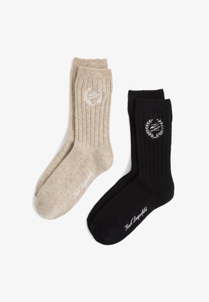 Two pairs of ribbed socks: one in beige with a logo design and one in black with a similar logo, both featuring a soft texture.