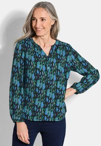 Langärmlige Bluse mit V-Ausschnitt, versehen mit einem mehrfarbigen abstrakten Muster in Grün, Blau und Schwarz, aus einem leichten Stoff gefertigt.