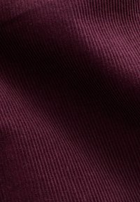 Primo piano di un tessuto in velluto a coste di colore viola scuro, che mostra la texture scanalata verticale e le pieghe morbide.