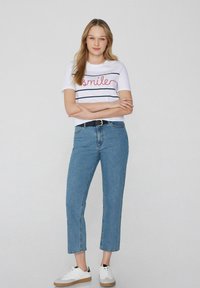 Camiseta blanca con texto rojo de "sonrisa" y rayas marinas, combinado con vaqueros de tiro alto azules claros y zapatillas blancas con suela de goma.