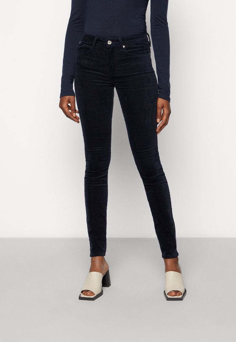 Marinblå kordjeans med hög midja, femficksdesign och knappstängning. Kombineras med ljusa blockklackade mules.