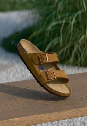 Hnědé semišové sandály na klínku s dvěma nastavitelnými popruhy, kovovými sponami a korkovou stélkou. Texturovaná černá podešev. Plochý design.