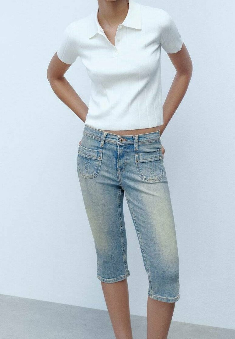 Polo blanca de canalé con mangas cortas combinada con pantalones capri de mezclilla azul claro con bolsillos delantero y trasero.