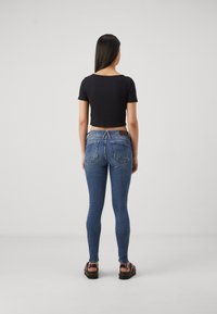 Smala blå jeans med medelhög midja, har bakfickor och en beige lapp. Kombineras med en åtsittande svart crop top och sandaler.