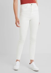 Vita högmidjade skinny jeans med en slät yta, med dragkedja, fem fickor och en smal passform. Bärs med vita sneakers.