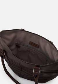 Brązowa skórzana torebka z otwartym zamkiem błyskawicznym, ukazująca wewnętrzną kieszeń na zamek oraz materiałową podszewkę z etykietą marki.