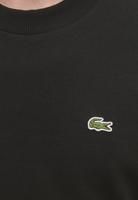 Pull en maille noire à col rond avec un petit logo crocodile vert brodé sur le côté gauche de la poitrine.