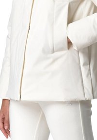 Weiße isolierte Jacke mit einem Frontreißverschluss und aufgesetzten Taschen, kombiniert mit enganliegenden weißen Hosen. Glatte Textur und minimalistisches Design.