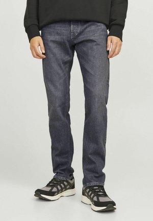 Jeans de mezclilla de color azul oscuro con corte recto, que presentan una textura desvanecida y costuras sutiles. Combinados con unas zapatillas deportivas negras.