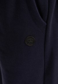 Marineblaue Sweatshirtmaterial mit strukturierten Oberflächen, mit einem runden schwarzen Stoff-Logopatch im Taschenbereich.