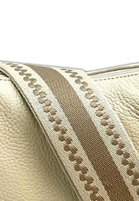 Beige Lederhandtasche mit einer strukturierten Oberfläche. Besitzt einen braunen, gemusterten Gurt mit helleren Akzenten, der ein gewebtes Design entlang seiner Kanten hervorhebt.