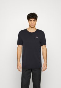 T-shirt nera a maniche corte in cotone, con collo rotondo e un piccolo logo FILA rosso e bianco sul lato sinistro del petto. Design semplice.