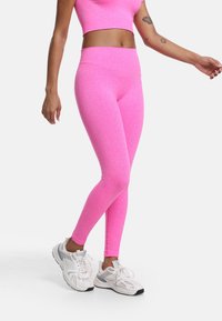 Jasnoróżowe legginsy wykonane z elastycznego, gładkiego materiału, z wysokim stanem i dopasowanym krojem, zestawione z białymi butami sportowymi.