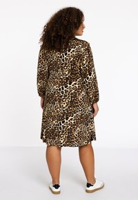 Leopardenmuster Kleid aus weichem Stoff, tailliert, mit langen Ärmeln und einem ausgestellten Rock. Kombiniert mit weißen Sneakers mit schwarzen Akzenten.